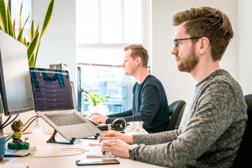 Two men in an office researching network monitoring tools on their computers